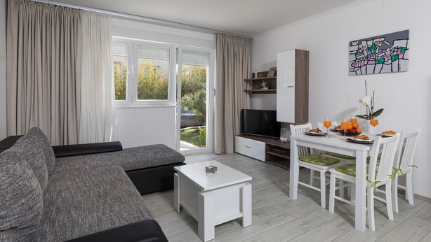 A modern living room with a grey sofa, a white coffee table, and a dining area with a white table and chairs.