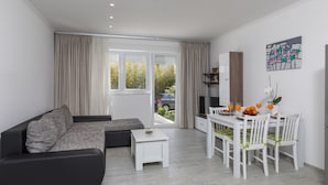 A modern living room with a sofa, a dining table with chairs, and a kitchen area.