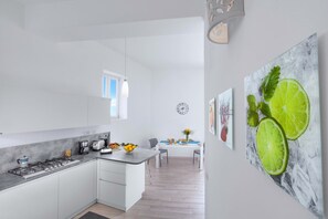 Una cocina moderna con estufa a gas, armarios blancos y un comedor con mesa y sillas.