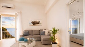 A modern living room with a sofa, a glass coffee table, a potted plant, and a painting of a boat.