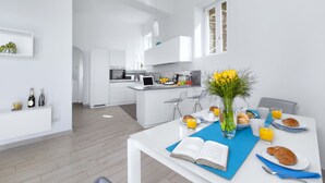 A modern kitchen with white cabinetry, a dining area with a table set for breakfast, and a view into the living space.