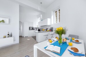 Eine moderne Küche mit weißen Schränken, ein Essbereich mit Frühstückstisch und Blick in den Wohnraum.
