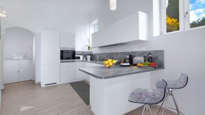 A modern kitchen with white cabinetry, a central island, bar stools, and a view of trees through a window.
