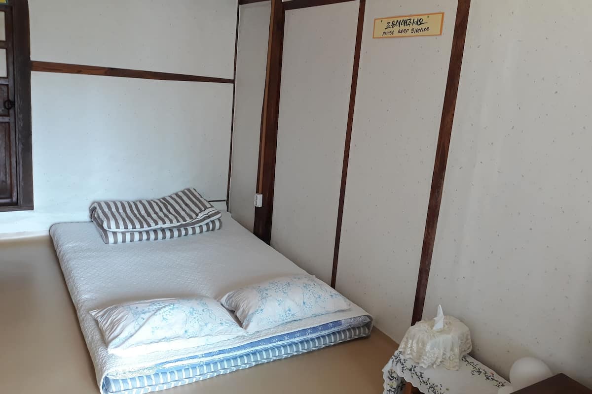 A single bed with striped and floral bedding, a small table with a decorative item, and a 'Please Keep Silence' sign on the wall.