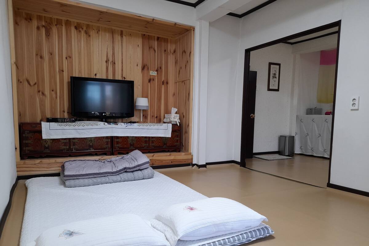 A bedroom with a wooden headboard, a television, a bedside table with a lamp, and a bed with pillows and a blanket.