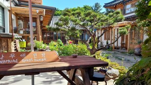 Ett traditionellt koreanskt gästhus med ett träbord och en träbänk, omgivet av krukväxter och en liten trädgård.