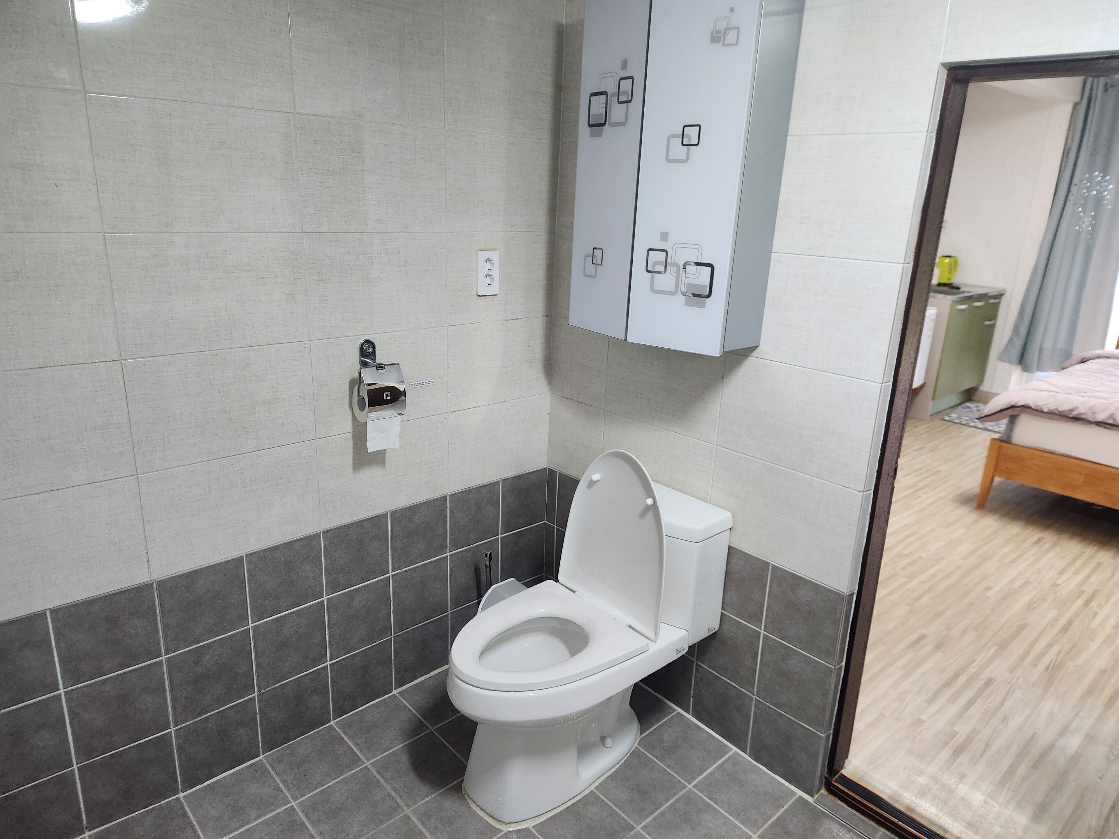 A modern bathroom with a toilet, a paper towel dispenser, and a cabinet with multiple compartments.