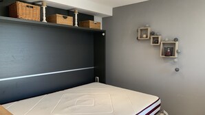 A bedroom with a bed, a shelf with baskets, and a wall-mounted shelf with decorative items. - Comfortable studio in the Gulf of St Tropez (Cavalaire-sur-Mer)