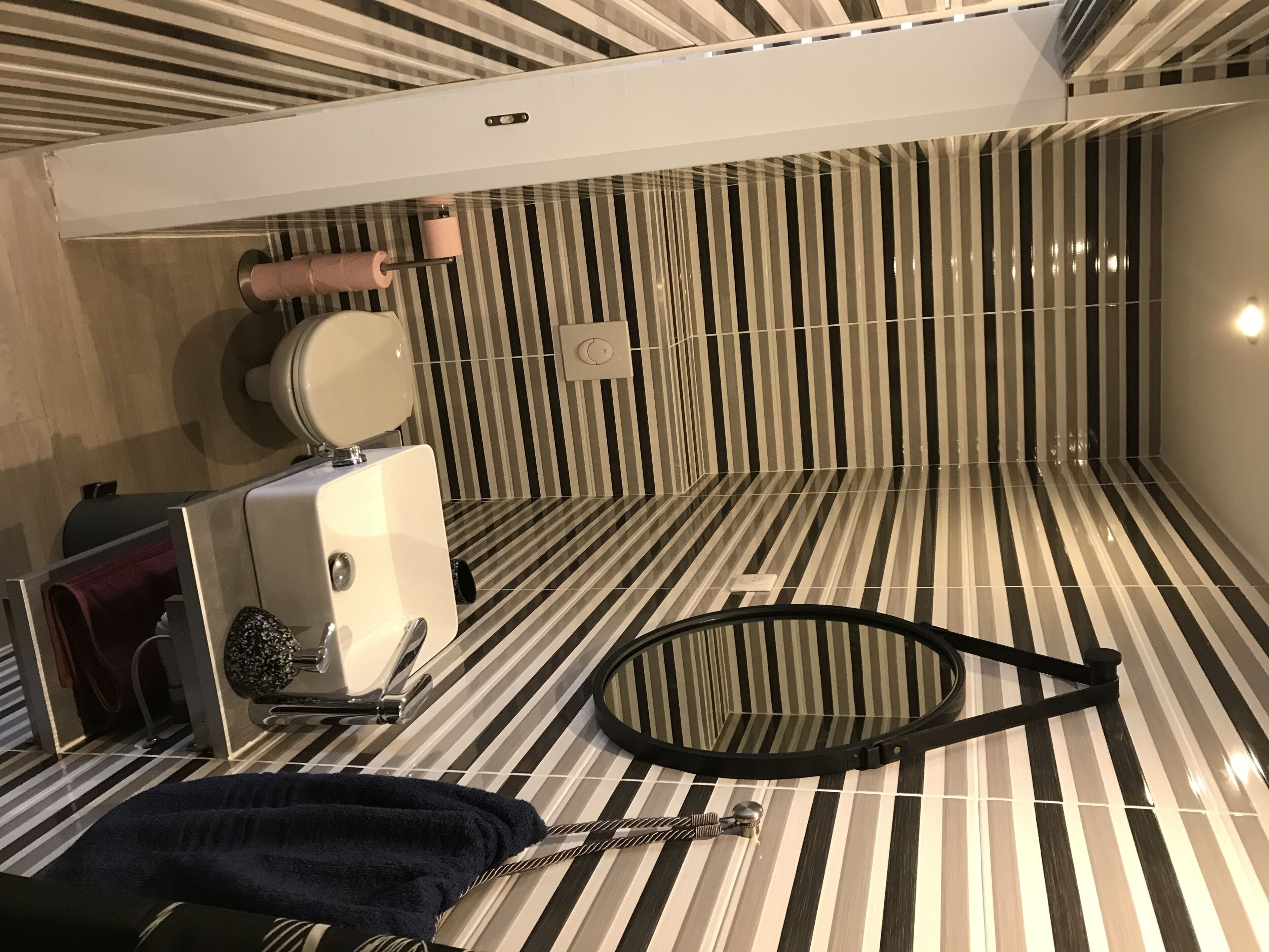Une salle de bain avec des murs recouverts de carreaux à rayures, des toilettes, un lavabo avec une serviette et un espace douche.