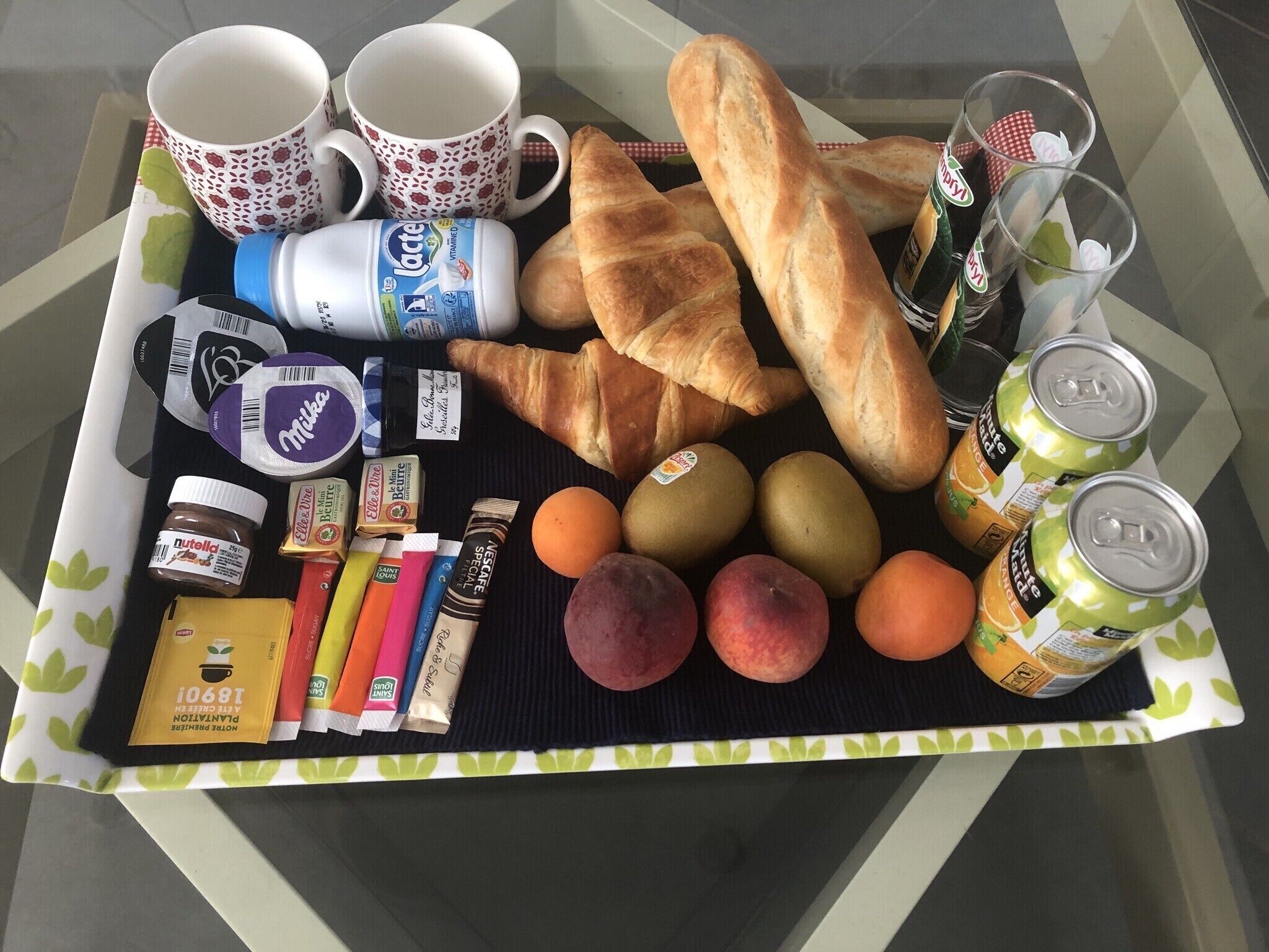 Een dienblad met eten, waaronder croissants, appels, perziken en Nutella.