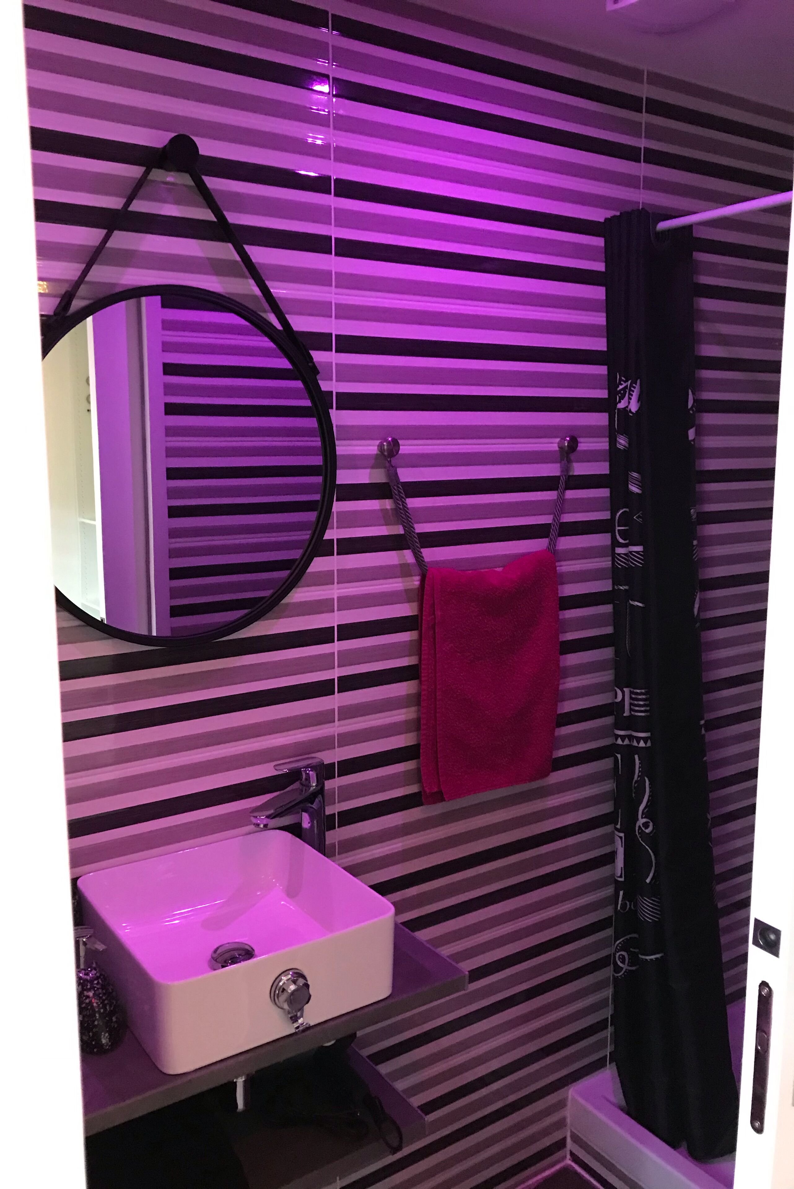 Ein Badezimmer mit gestreifter Wand, einem weißen Waschbecken, einem Spiegel und einem Handtuchhalter mit einem roten Handtuch.