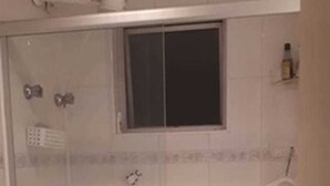 A small, tiled bathroom with a toilet, a shower stall, and a window. - Apartamento Itaim Bibi (São Paulo)