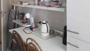 A compact kitchen with white cabinets, a dining table with chairs, and various kitchen appliances. - Apartamento Itaim Bibi (São Paulo)