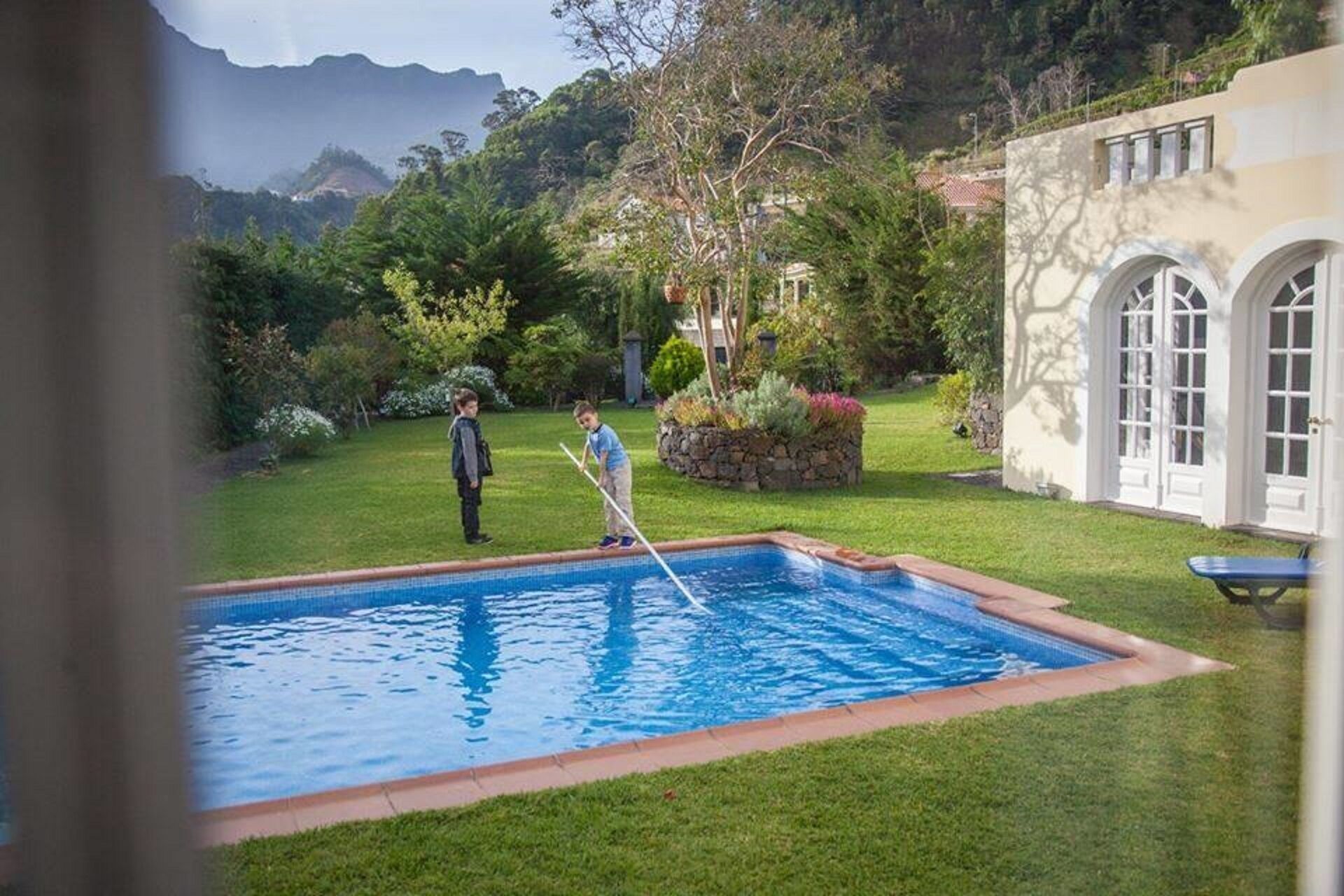 Piscina com gramado, vaso de pedra e um edifício com janelas em arco.