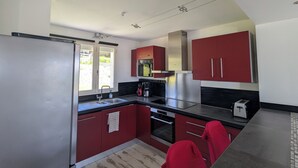 Een moderne keuken met rode kastjes, roestvrijstalen apparatuur en een groot raam dat voor natuurlijk licht zorgt.