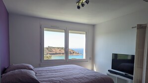 Een slaapkamer met een bed, een televisie, een raam met uitzicht op zee en een plafondlamp.
