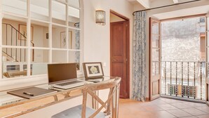 Een kamer met een bureau, laptop en een lijst met foto. Er is een deur naar een balkon met een hekwerk.