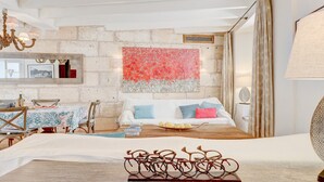 Een gezellige kamer met een rustieke stenen muur, een bed met kleurrijke kussens, een zithoek met een tafel en stoelen, en een kroonluchter.