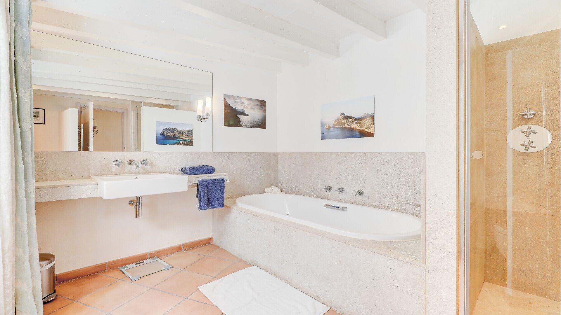 A modern bathroom with a sink, mirror, and bathtub. There are two framed pictures on the wall.