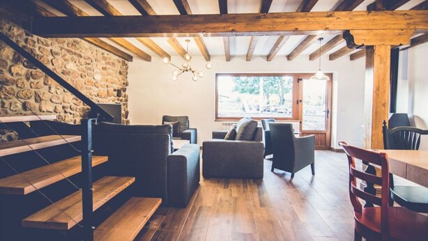 A rustic interior with exposed wooden beams, a stone wall, and a cozy seating area with a fireplace.