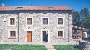 A stone building with a red-tiled roof, multiple windows, and a central entrance.