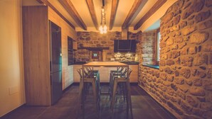 A kitchen with a stone wall, wooden beams, a central island with bar stools, and a built-in TV.