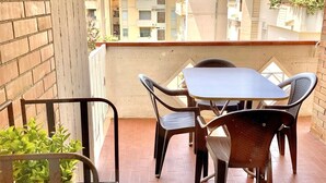Un balcon avec une table et des chaises, des plantes en pot et une vue sur les bâtiments et les montagnes.