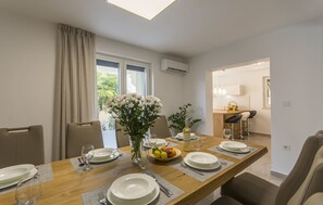 A dining area with a wooden table set for four, a vase of flowers, and a fruit bowl. - Charming villa just 3 minutes from the beach (Porec)