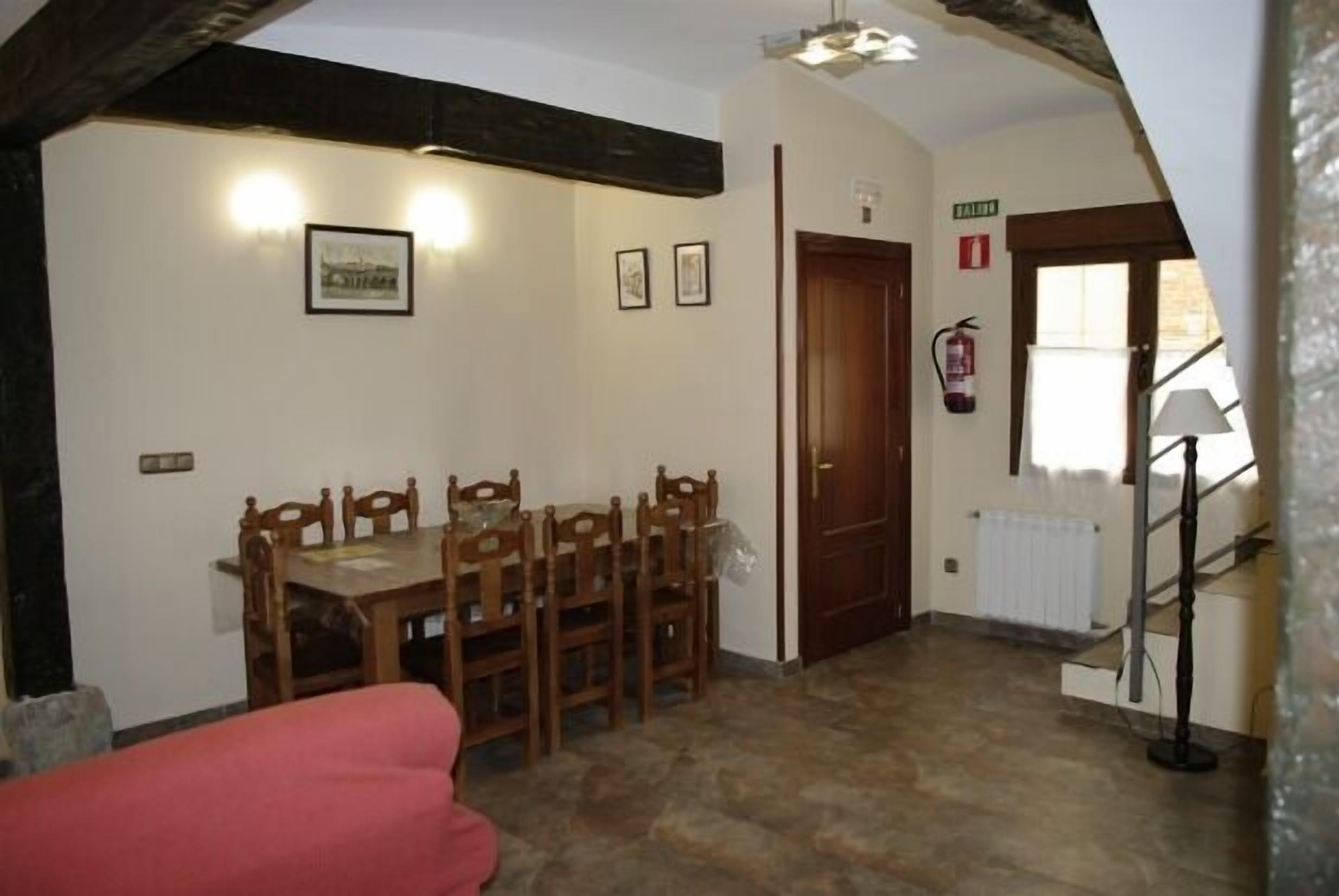 A dining area with a wooden table and chairs, a red sofa, and a staircase leading to an upper floor.