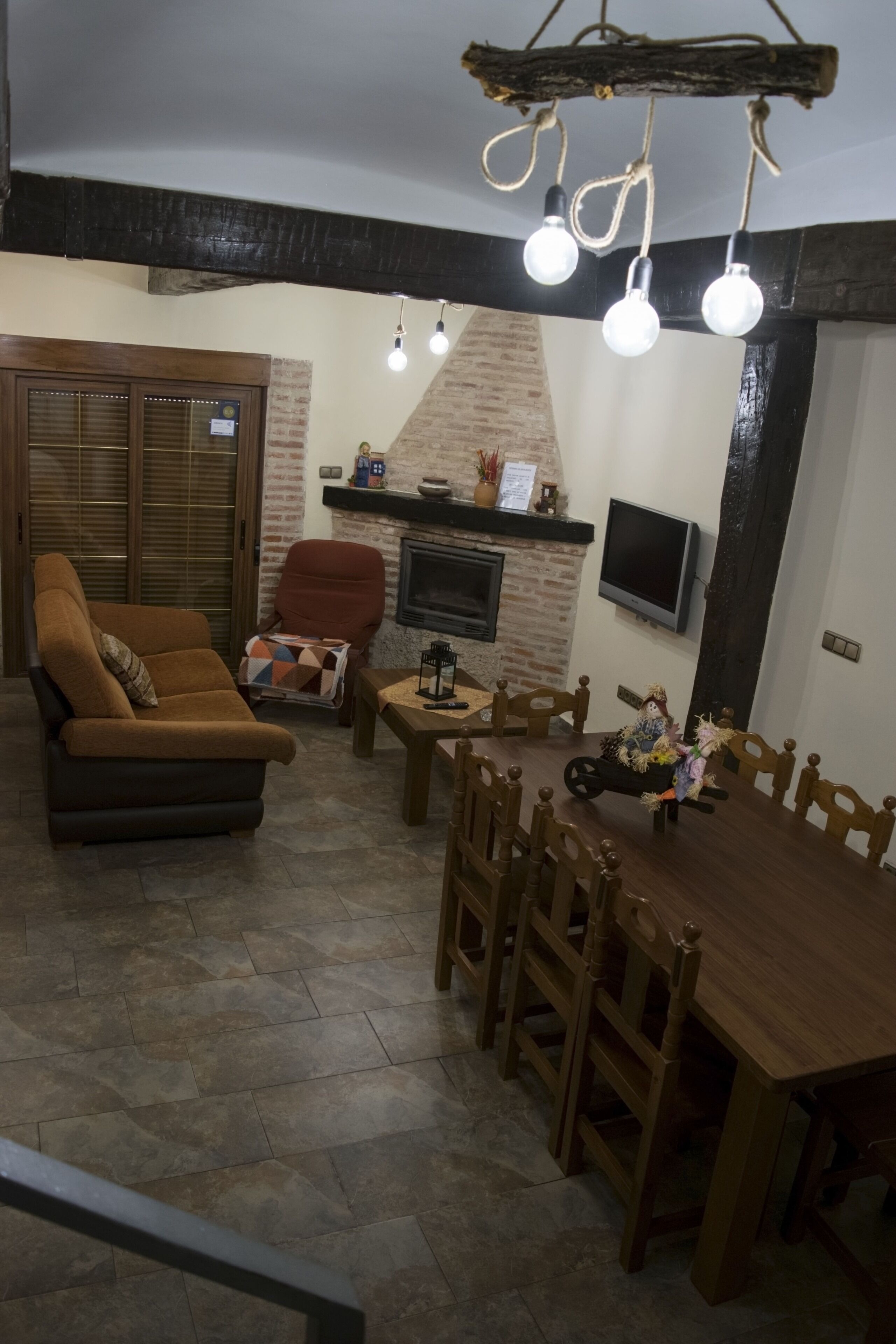Un salon comprenant un canapé, une table à manger avec des chaises, une cheminée et un téléviseur fixé au mur.