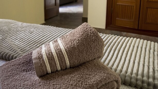 Een net opgemaakt bed met een bruine gevouwen handdoek en een gestreepte handdoek.