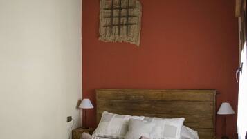 A bedroom with a wooden bed, two bedside lamps, a red wall, and a rustic ceiling.