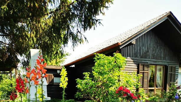 A garden with a wooden cabin, a white pillar, and various flowers. - MERIKOTKA: cozy wooden cottage sLOVEnia with farm view & wonderful neighborhoods (Braslovče)