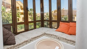 A room with a large window, a cushioned bench, and a woven mat.