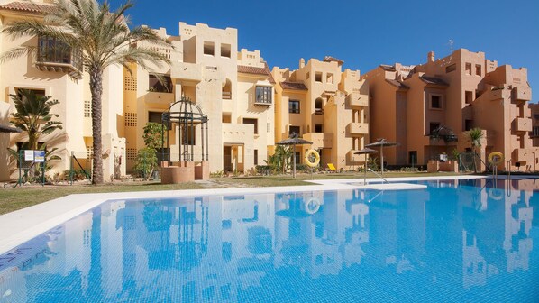 A swimming pool with a clear blue water surface, surrounded by buildings with a beige facade and balconies.