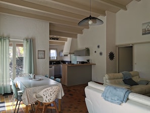Ampla sala de estar com mesa de jantar, sofá e cozinha ao fundo.