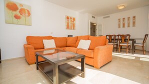 Un salon avec un canapé orange, une table basse en verre et un coin repas comprenant des chaises et une table en bois.