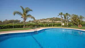 Une piscine d’un bleu éclatant, agrémentée d’un bord décoratif, entourée de palmiers et de verdure, avec un paysage vallonné en arrière-plan.