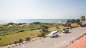 Un espace de stationnement avec un fourgon blanc, une voiture bleue et un petit bâtiment blanc situé près de la plage.