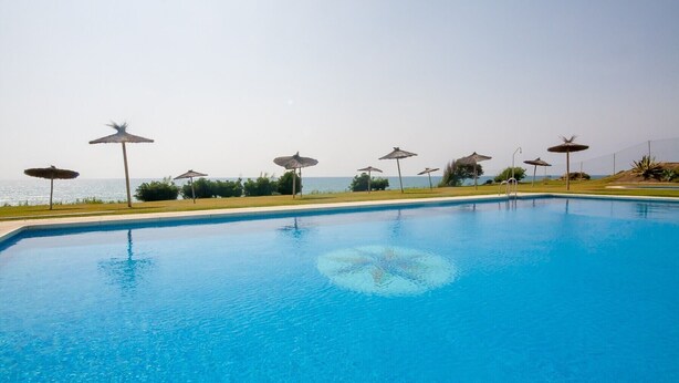 Une piscine à l’eau d’un bleu cristallin, entourée de parasols et offrant une vue sur la mer.