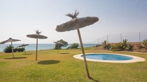 Un espace piscine offrant une vue dégagée sur l’océan, entouré de pelouse et agrémenté de parasols en chaume.