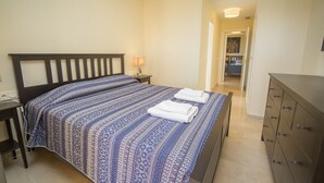 A neatly made bed with a patterned bedspread, a bedside lamp, and a dresser with multiple drawers. - Coto Real Andros 201 (Manilva)