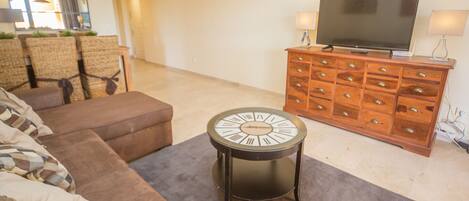 Un salon avec un canapé marron, une horloge ronde, un meuble en bois doté de tiroirs et un téléviseur à écran plat.