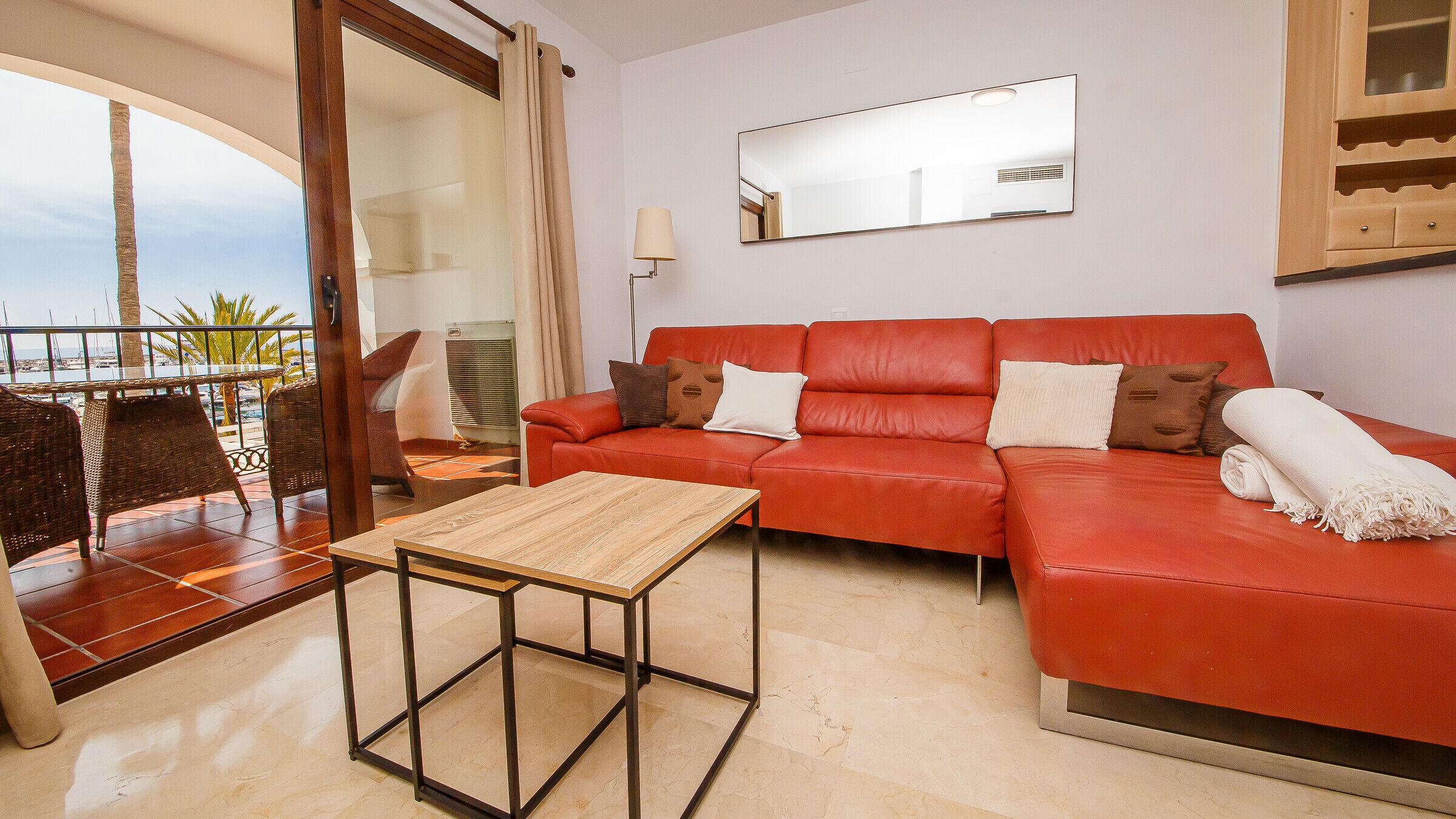 Un salón con sofá rojo, una mesa de centro de madera y un balcón con vistas al mar.