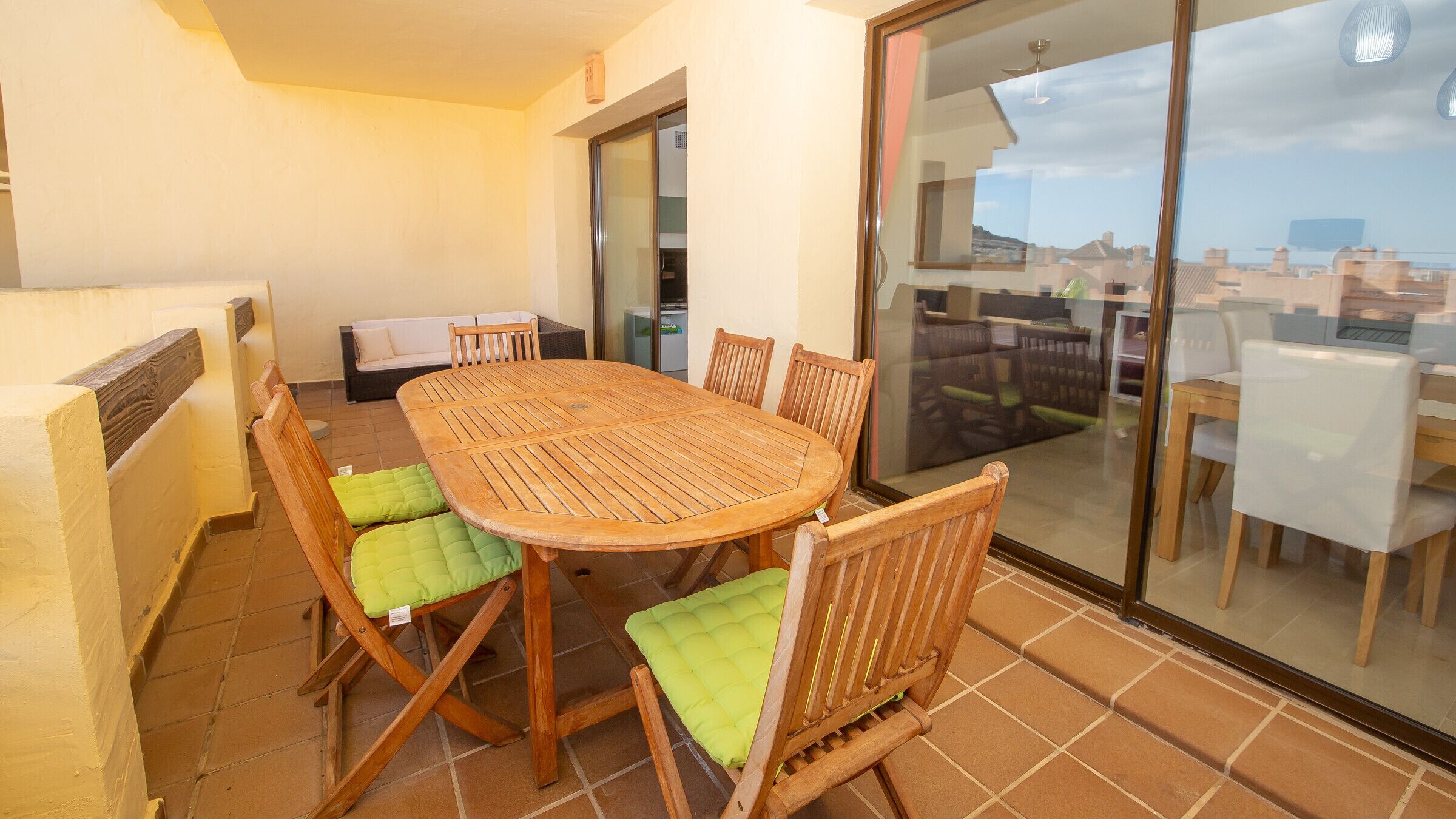 A wooden table with six chairs, a sofa, and a sliding glass door leading to a balcony with a city view.