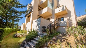 A multi-story building with a staircase leading to the entrance, surrounded by greenery and a clear sky. - Coto Real 102 Khios. (Manilva)