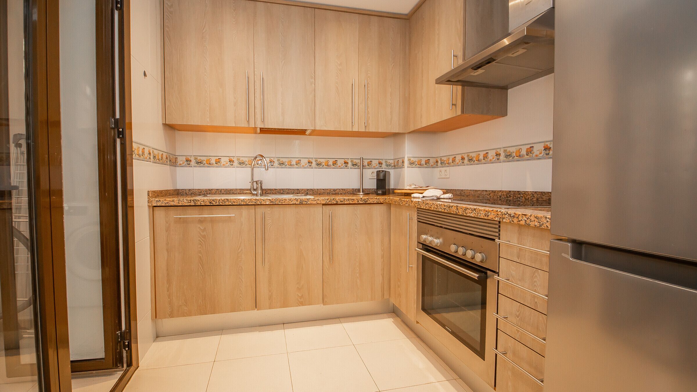 Una cocina con armarios de madera, un refrigerador de acero inoxidable y salpicadero de azulejos.