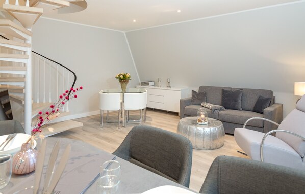 A modern living room with a staircase, a dining area, and a grey sofa. - Penthouse maisonette Lagmöwe (Westerland)