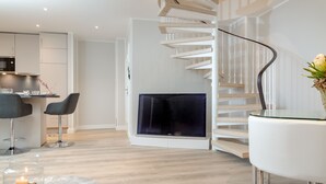 A modern living room with a spiral staircase, a flat-screen TV, and a dining area with two chairs. - Penthouse maisonette Lagmöwe (Westerland)