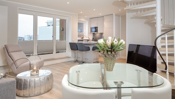 A modern living room with a glass coffee table, a comfortable sofa, and a TV. - Penthouse maisonette Lagmöwe (Westerland)